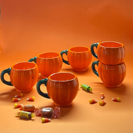 Madcap Cottage set of six orange pumpkin halloween coffee mugs on an orange background with halloween candy.