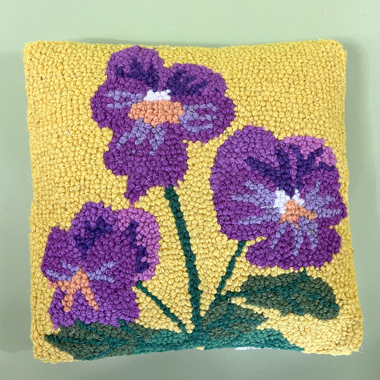 A spring pillow with purple pansies on a yellow background. 