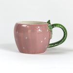 a pink ceramic strawberry mug with a green leafy handle