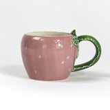 a pink ceramic strawberry mug with a green leafy handle