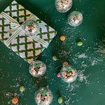 six silver disco ball christmas ornaments on a snow covered green background