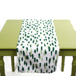 Green and white table runner with abstract green brushstroke dots displayed on a light green table.