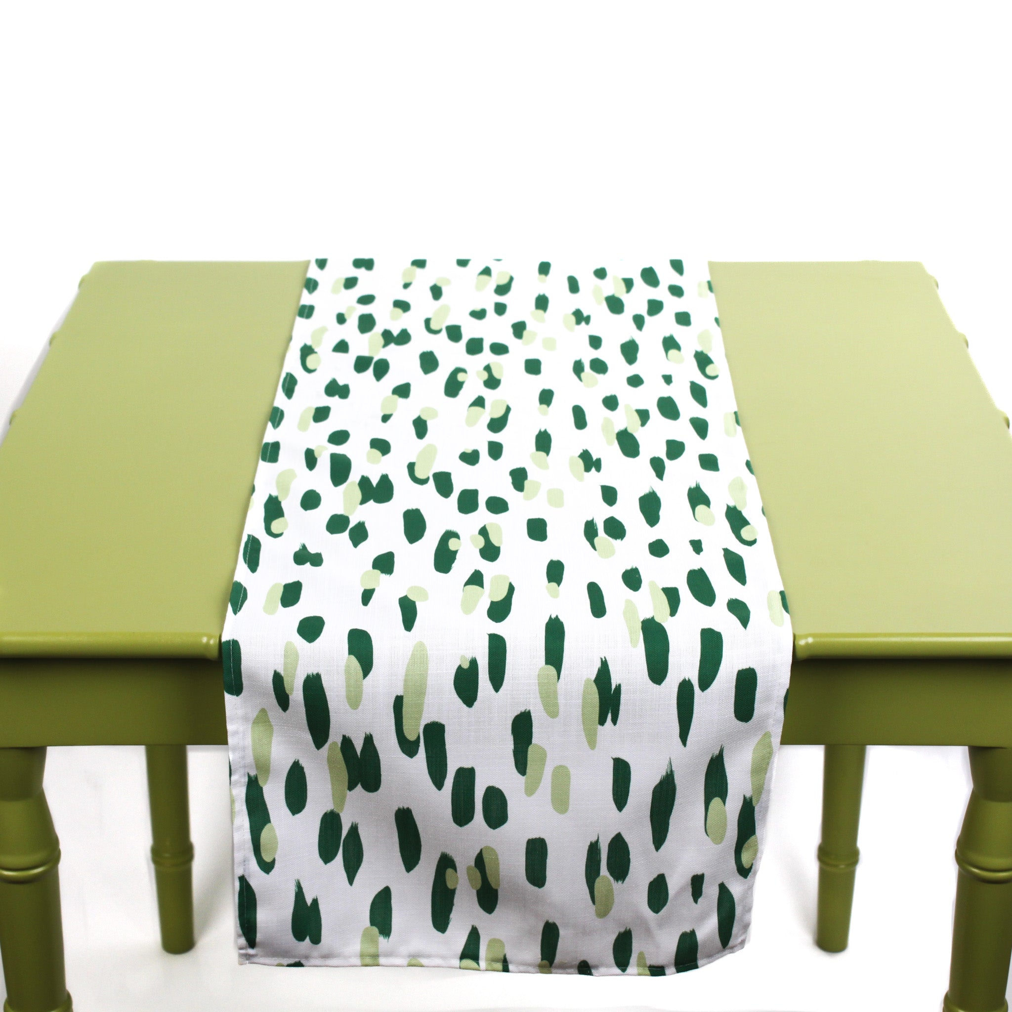 Green and white table runner with abstract green brushstroke dots displayed on a light green table.