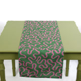 Green and pink abstract patterned table runner laid across a light green table.