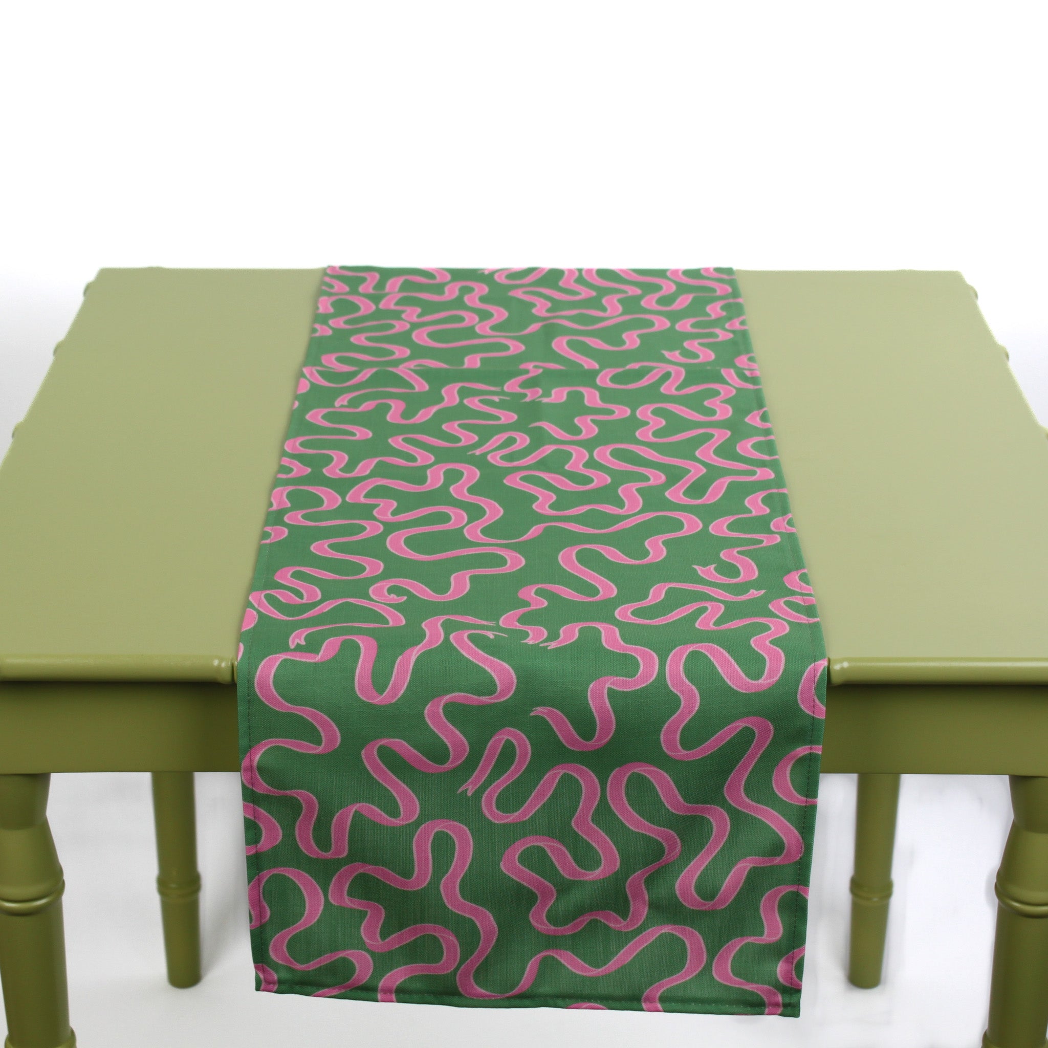 Green and pink abstract patterned table runner laid across a light green table.