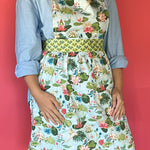 a woman wearing a green, pink and blue floral apron featuring the Meadow bluc water lilies pattern fabric from madcap cottage