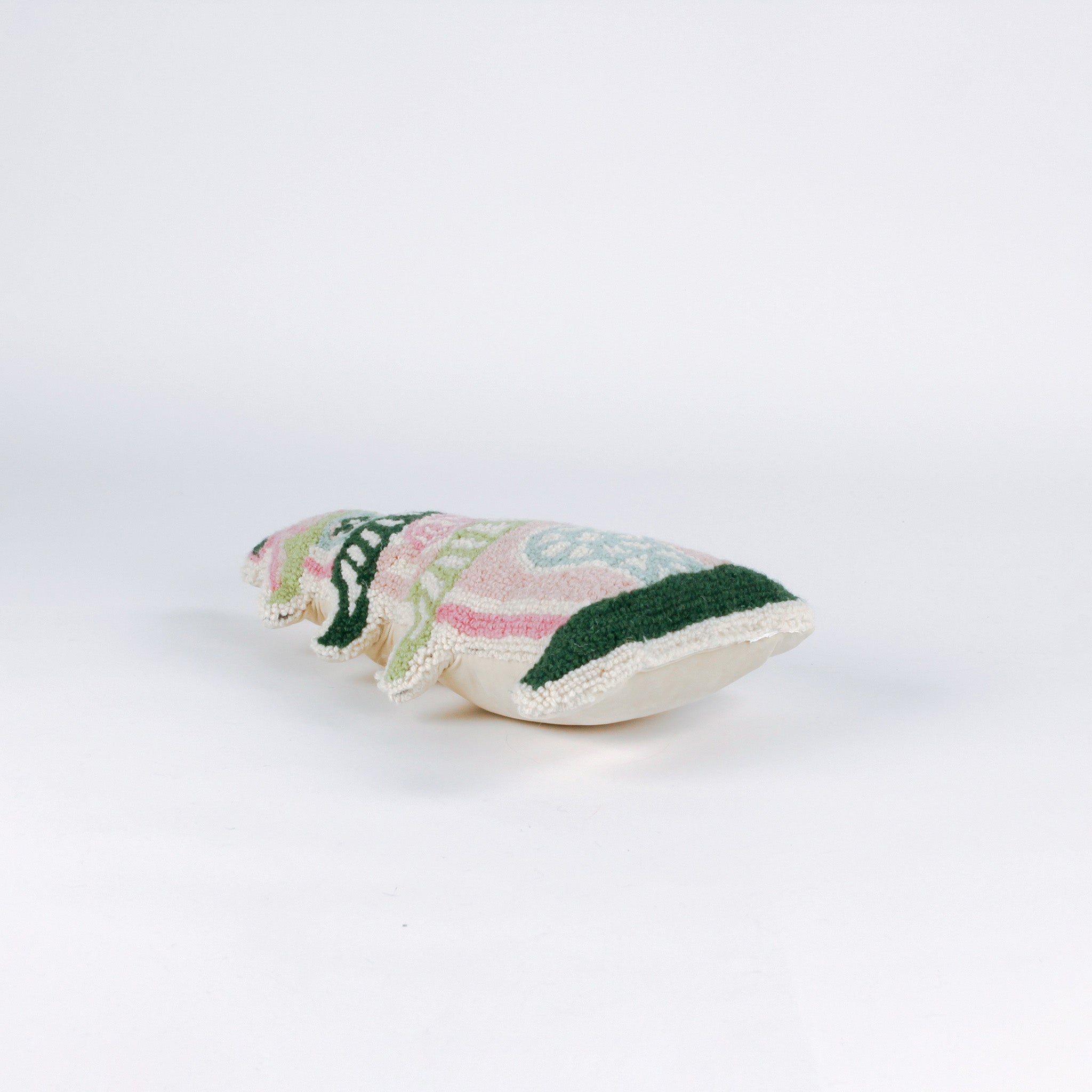 side of a Decorative pillow shaped like a pagoda, featuring a pink base with green and white tiered roofs and intricate embroidered details in soft pastel colors.