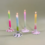 Four ceramic candle holders with scalloped edges holding pastel taper candles with four different patterns