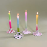 Four ceramic candle holders with scalloped edges holding pastel taper candles with four different patterns