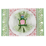 pink and green paper placemats in a trellis pattern called "Monserrat" by Madcap Cottage with white background. A white plate is placed on top of it with a cloth and a santa napkin ring