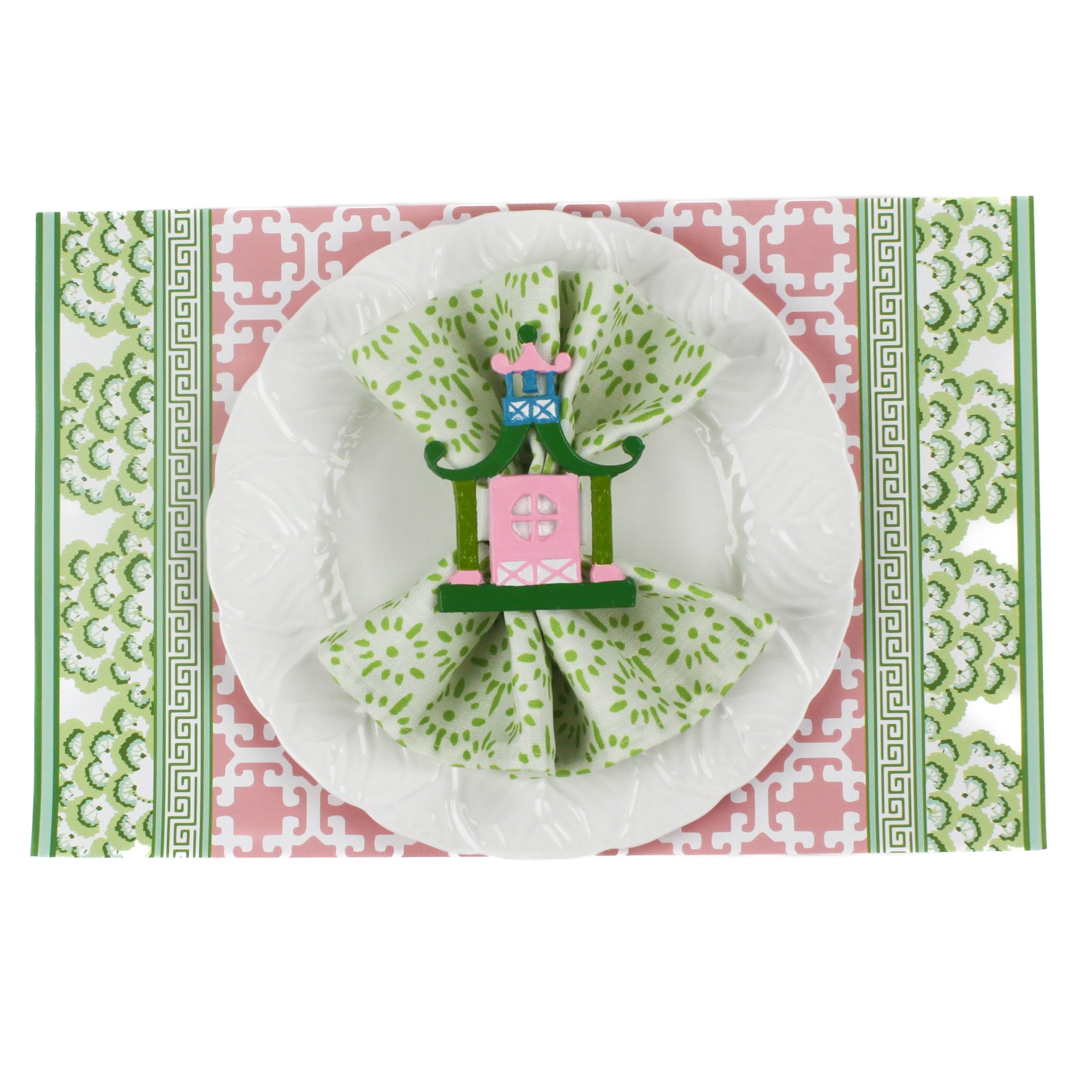 pink and green paper placemats in a trellis pattern called "Monserrat" by Madcap Cottage with white background. A white plate is placed on top of it with a cloth and a santa napkin ring