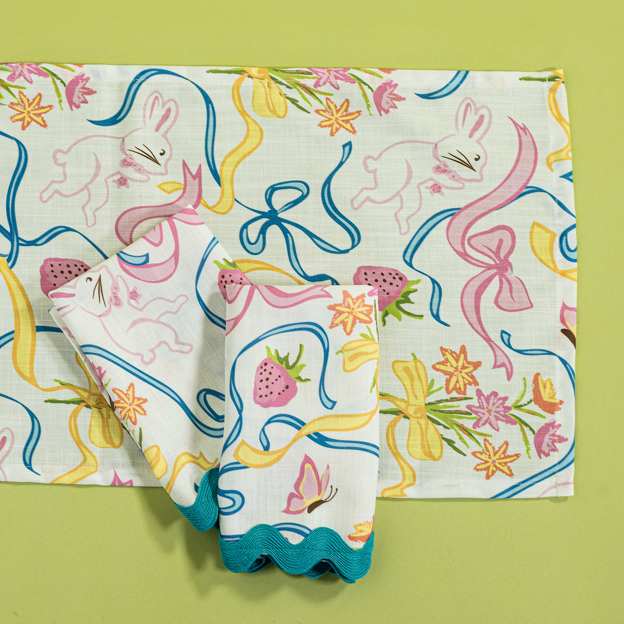 a multicolored bunnies and bow print table runner and napkin in a  bunny and bow print fabric with ric rac trim.