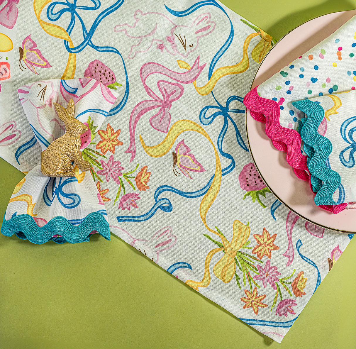 a multicolored bunnies and bow print cloth table runner and napkins on a plate