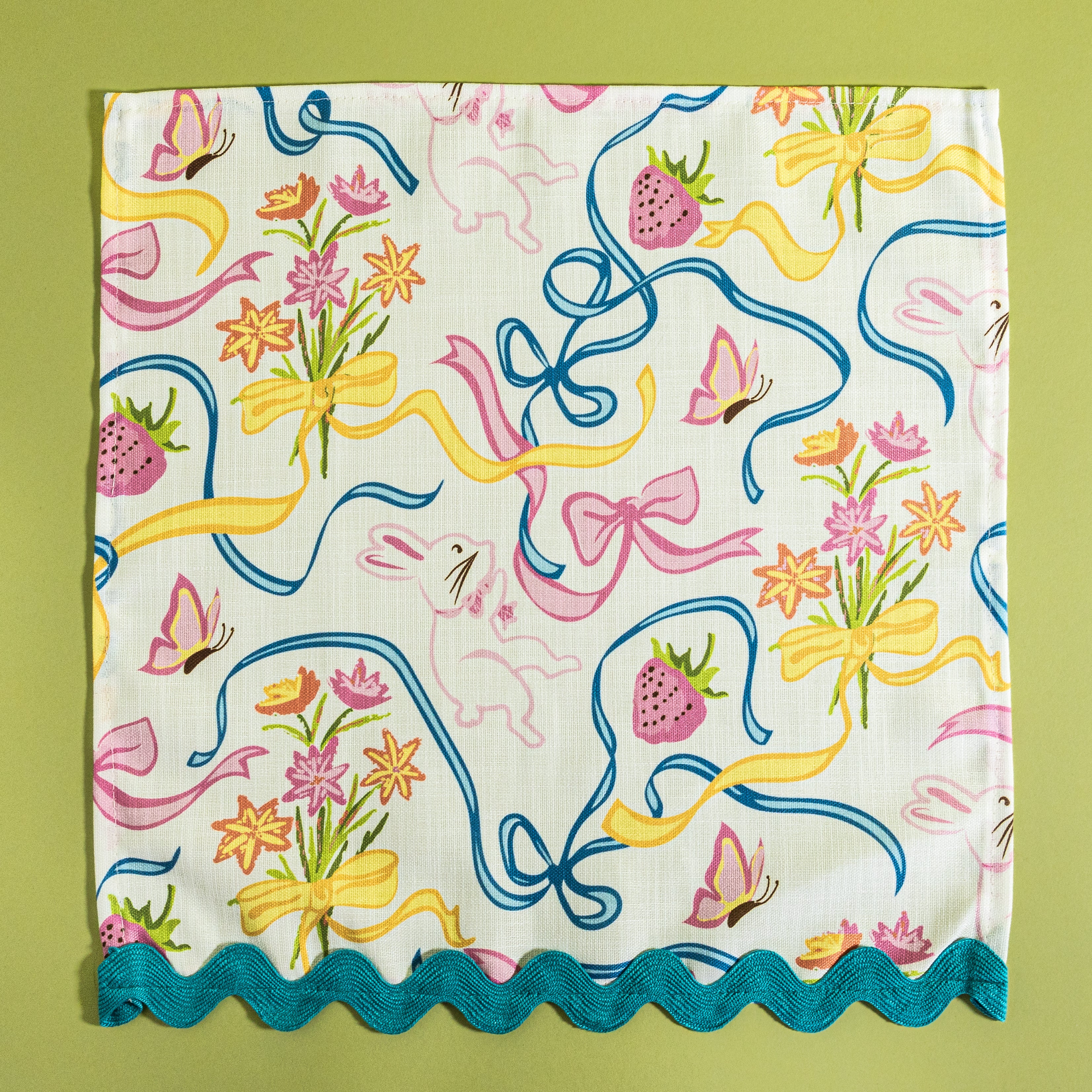 A Springtime bunnies and bow print cloth dinner napkin in multicolor with a blue ric rac trim against a light green background.