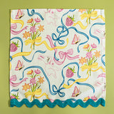 A Springtime bunnies and bow print cloth dinner napkin in multicolor with a blue ric rac trim against a light green background.