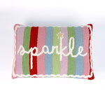 Rectangular colorful-pillow with colorful vertical stripes in red, pink, green, blue, and lavender, featuring the word “sparkle” written in white cursive with a small gold star above the letter “k.”