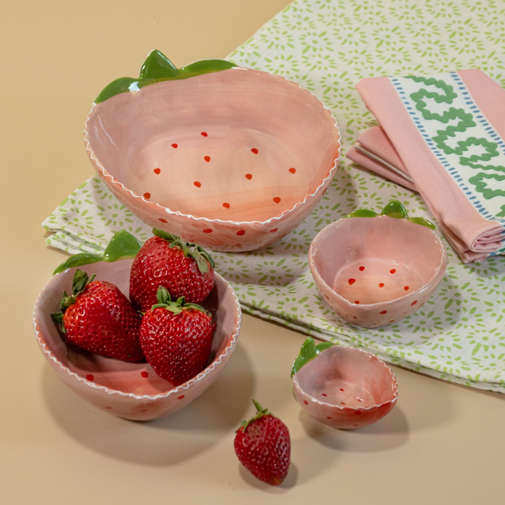 A group of four nested pink ceramic strawberry dishes filled with strawberries and resting on green and white napkins from madcap cottage.