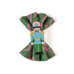 a pink and green napkin inside a metal blue, pink and green nutcracker shaped christmas napkin ring on a white background. 