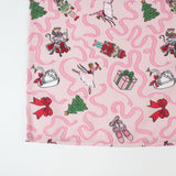 a pink christmas table runner featuring a pattern of colorful nutcracker related motifs on a white background. 