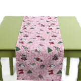 Pink Christmas-themed table runner with playful holiday icons displayed on a green table.
