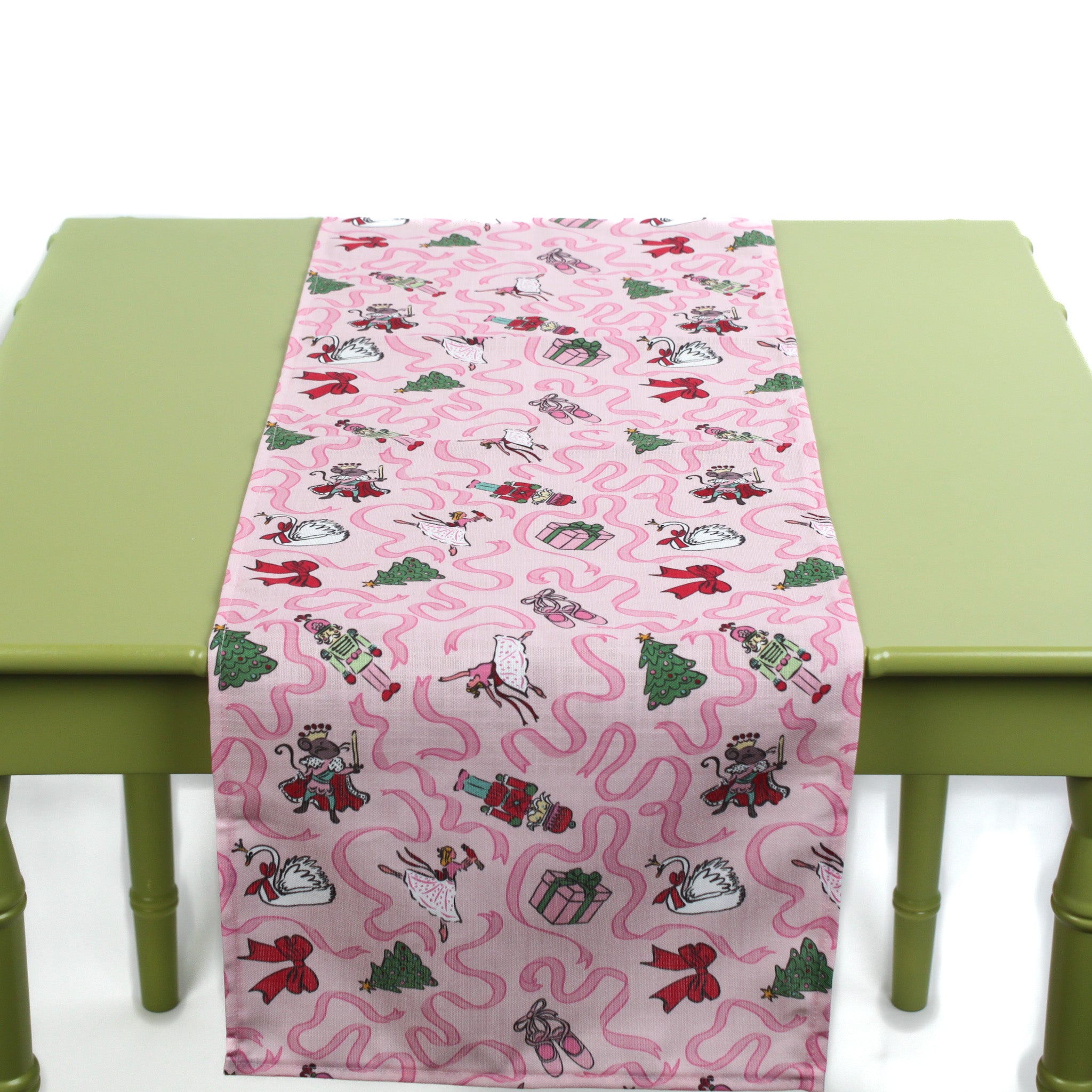 Pink Christmas-themed table runner with playful holiday icons displayed on a green table.