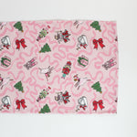 a pink christmas table runner featuring a pattern of colorful nutcracker related motifs on a white background. 