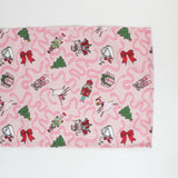 a pink christmas table runner featuring a pattern of colorful nutcracker related motifs on a white background. 