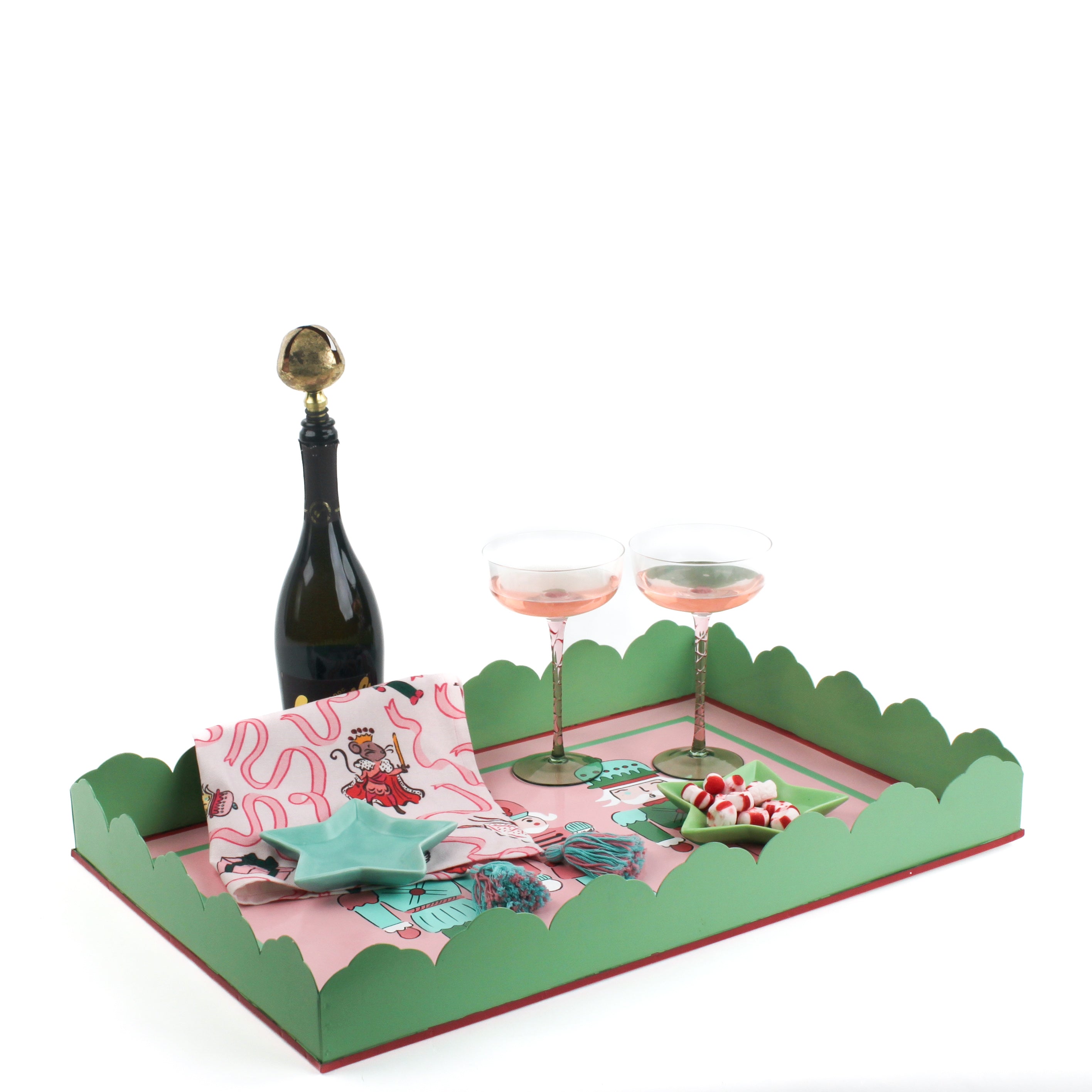 A pink and green nutcracker christmas tray filled with a pink christmas napkin, a blue star dish, two pink champagne coupes and a bottle of champagne.