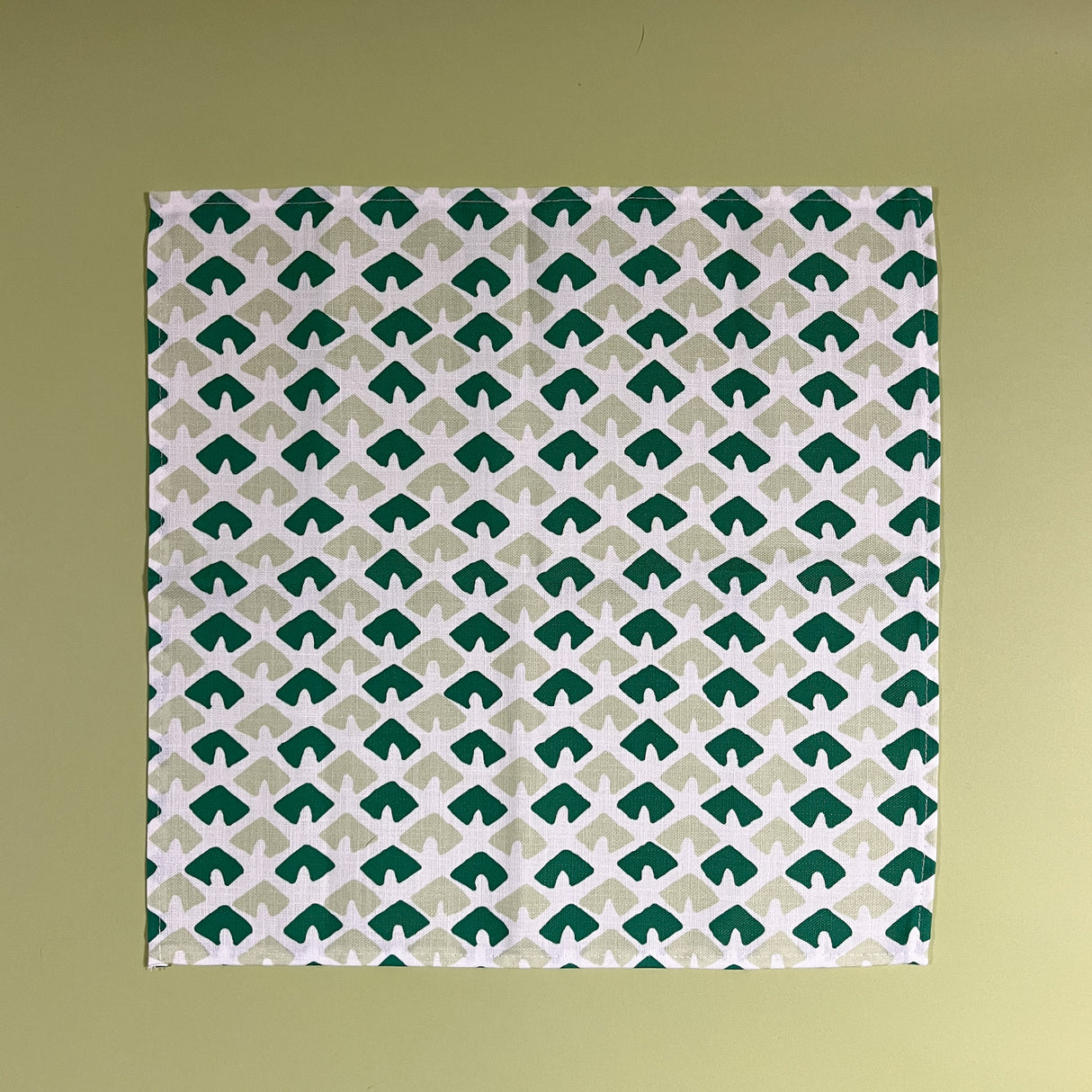 a white and green dinner napkin featuring a triangular block print motif called Old Jaipur from Madcap Cottage. 