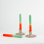 2 orange and green taper candles in white ceramic candle holders and 1 candle lying down