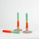 2 orange and green taper candles in white ceramic candle holders and 1 candle lying down