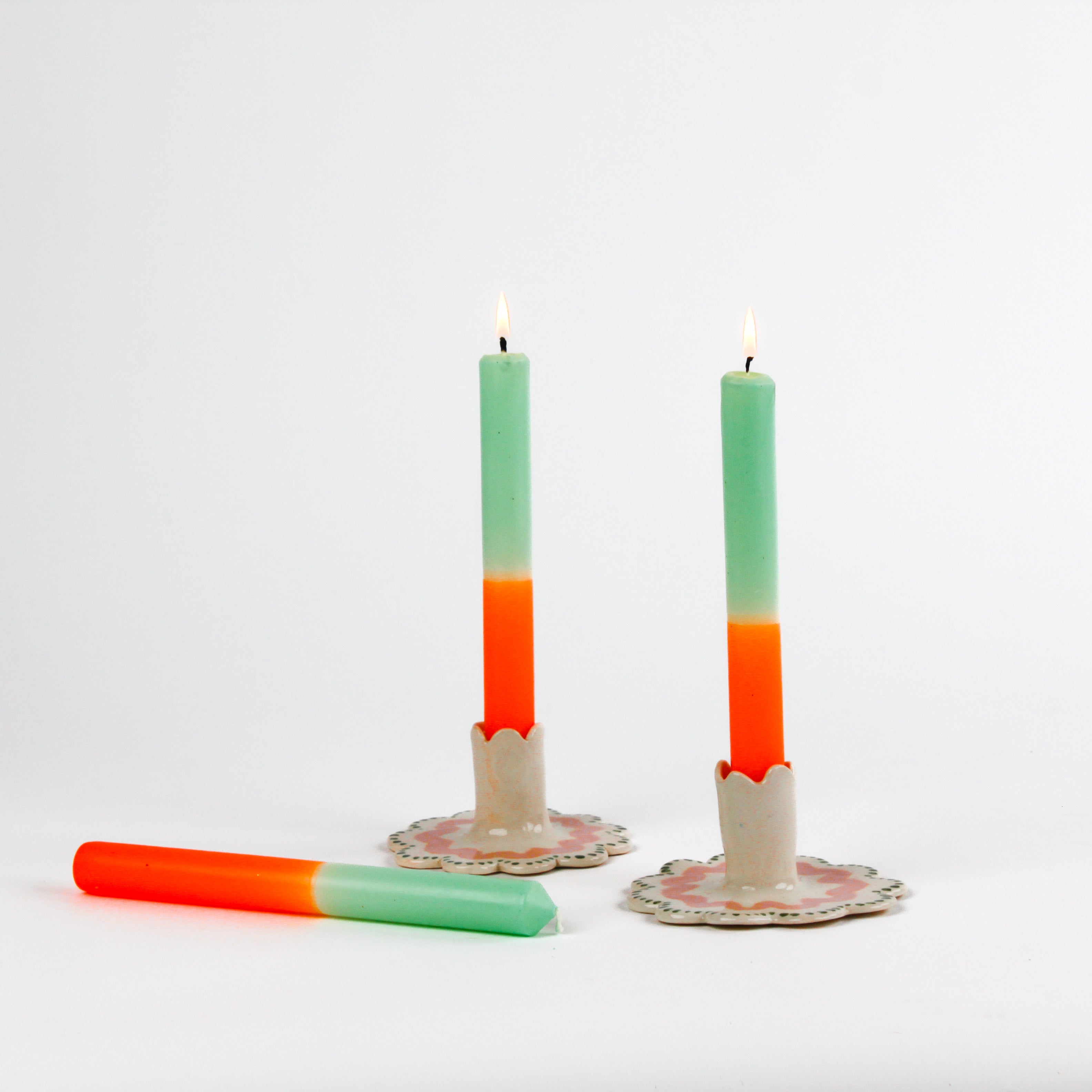 2 orange and green taper candles in white ceramic candle holders and 1 candle lying down
