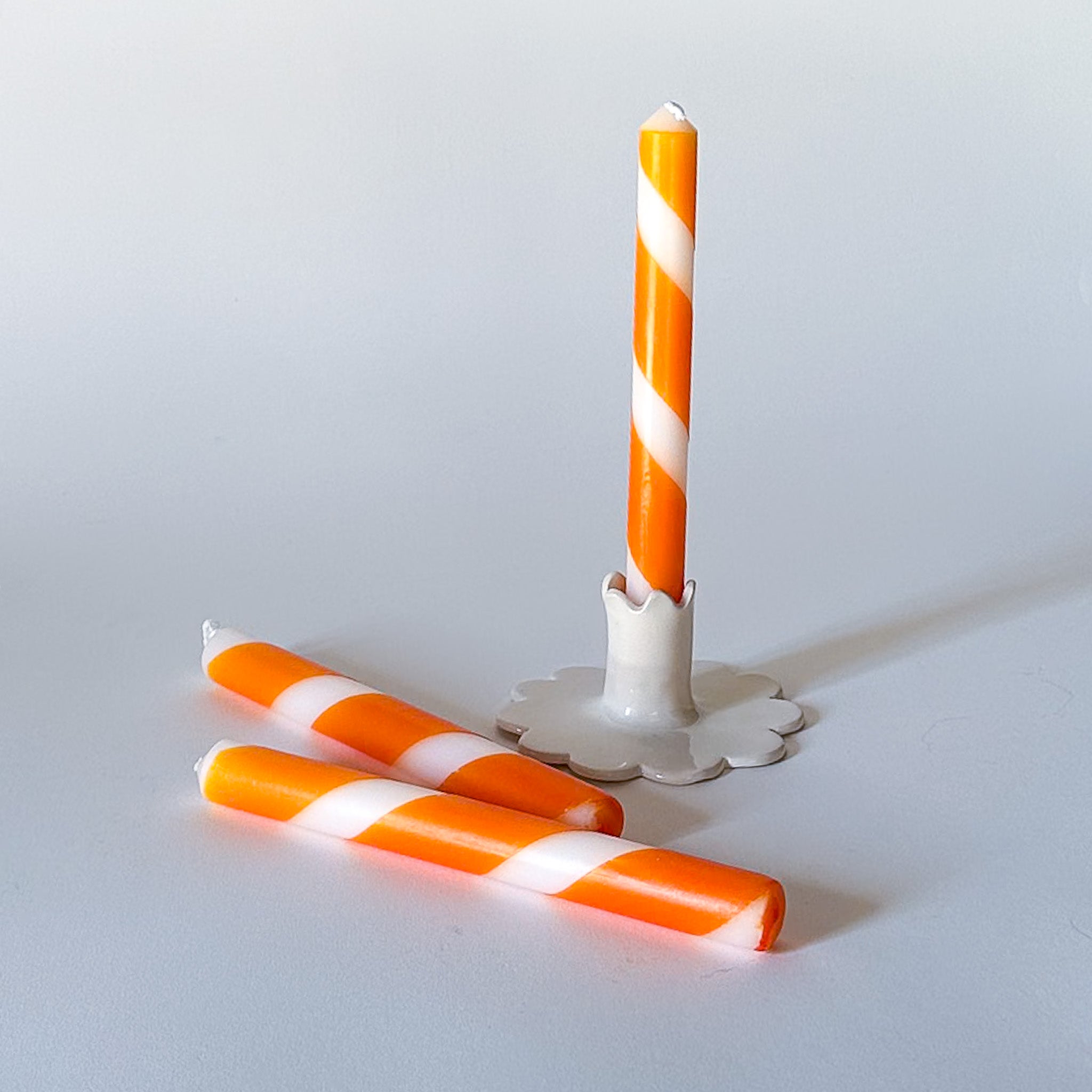 Three orange and white stripe taper candles, with one upright and two lying down, on a white background.