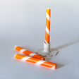 Three orange and white stripe taper candles, with one upright and two lying down, on a white background.