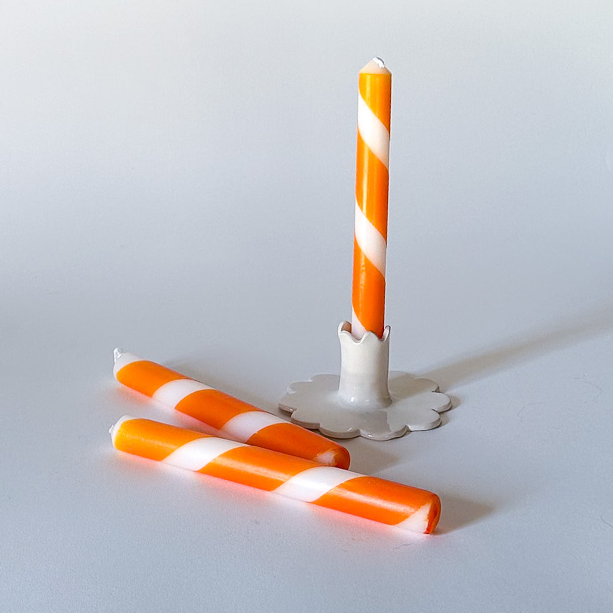 Three orange and white stripe taper candles, with one upright and two lying down, on a white background.