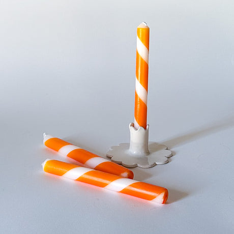 Three orange and white stripe taper candles, with one upright and two lying down, on a white background.