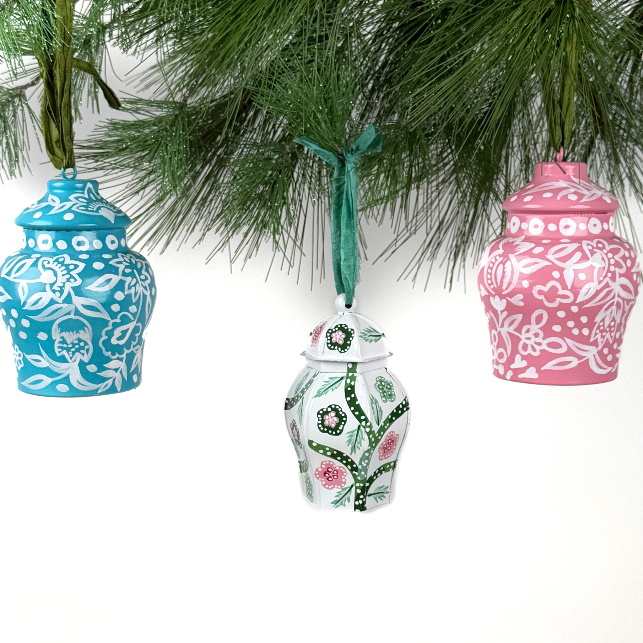 Set of three hand-painted ginger jar Christmas ornaments in blue, green, and pink hanging from pine branches, chinoiserie holiday decor.
