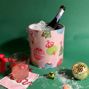 A pink ice bucket decorated with ornament motifs and filled with ice and a champagne bottle