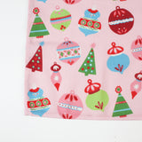 a pink christmas table runner featuring a pattern of colorful ornaments on a white background. 