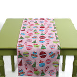 Pink table runner featuring festive ornament designs laid across a light green table.