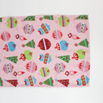 a pink christmas table runner featuring a pattern of colorful ornaments on a white background. 