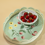 an oval tole tray carrying a white bowl full of strawberrieis and a base featuring motifs of strawberries and yellow flowers