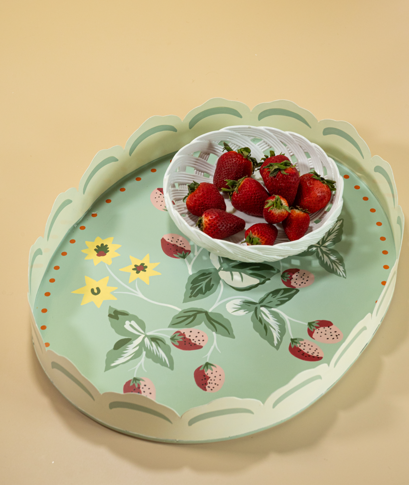 an oval tole tray carrying a white bowl full of strawberrieis and a base featuring motifs of strawberries and yellow flowers