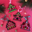 four pink felt chinoiserie christmas ornaments in the shape of pagodas against a red background 