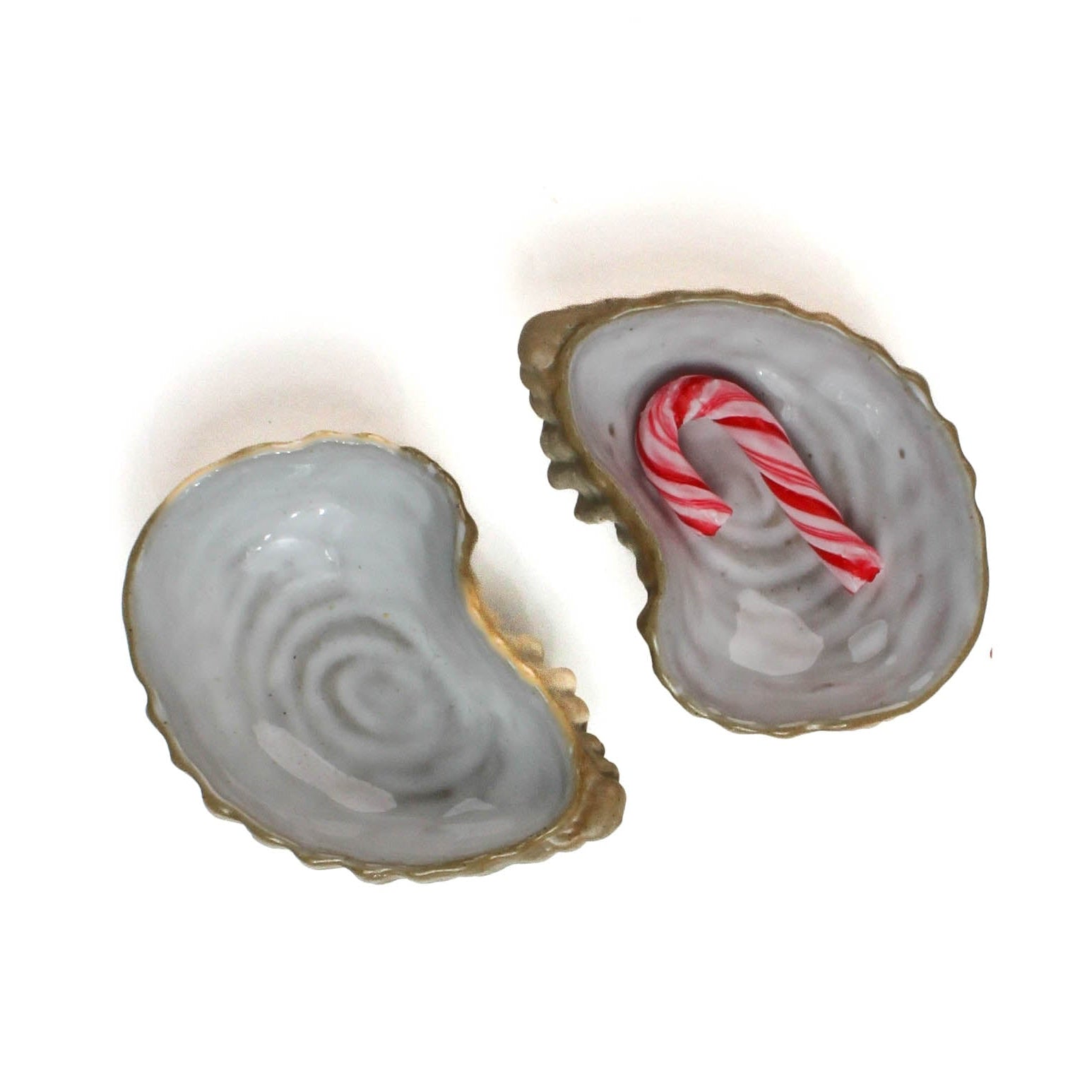 Two ceramic oyster shells with shellfish on a white background, 1 with candy cane on it