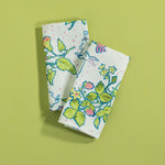 A folded pair of multicolor Springtime Strawberry print cloth dinner napkins against a green background.