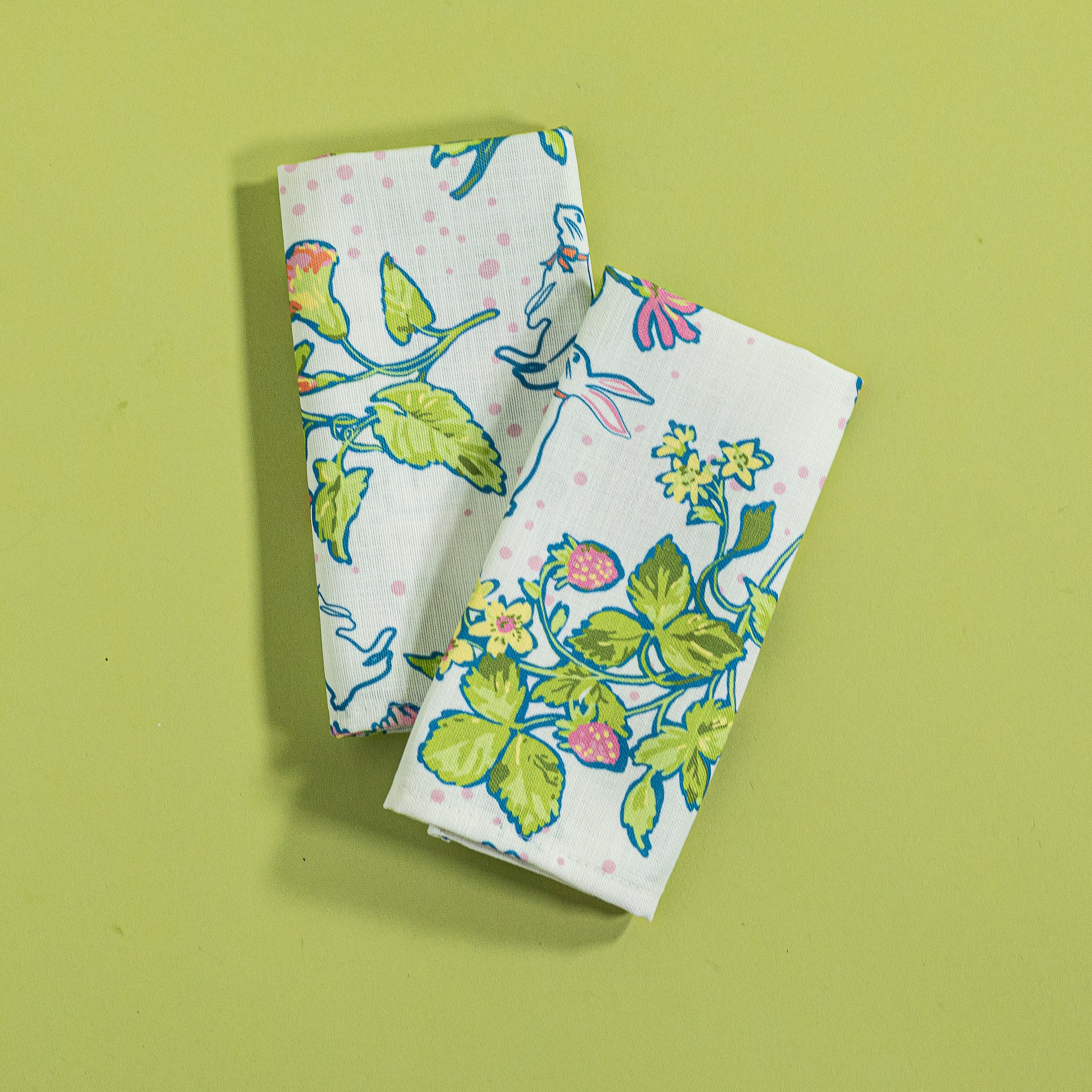 A folded pair of multicolor Springtime Strawberry print cloth dinner napkins against a green background.