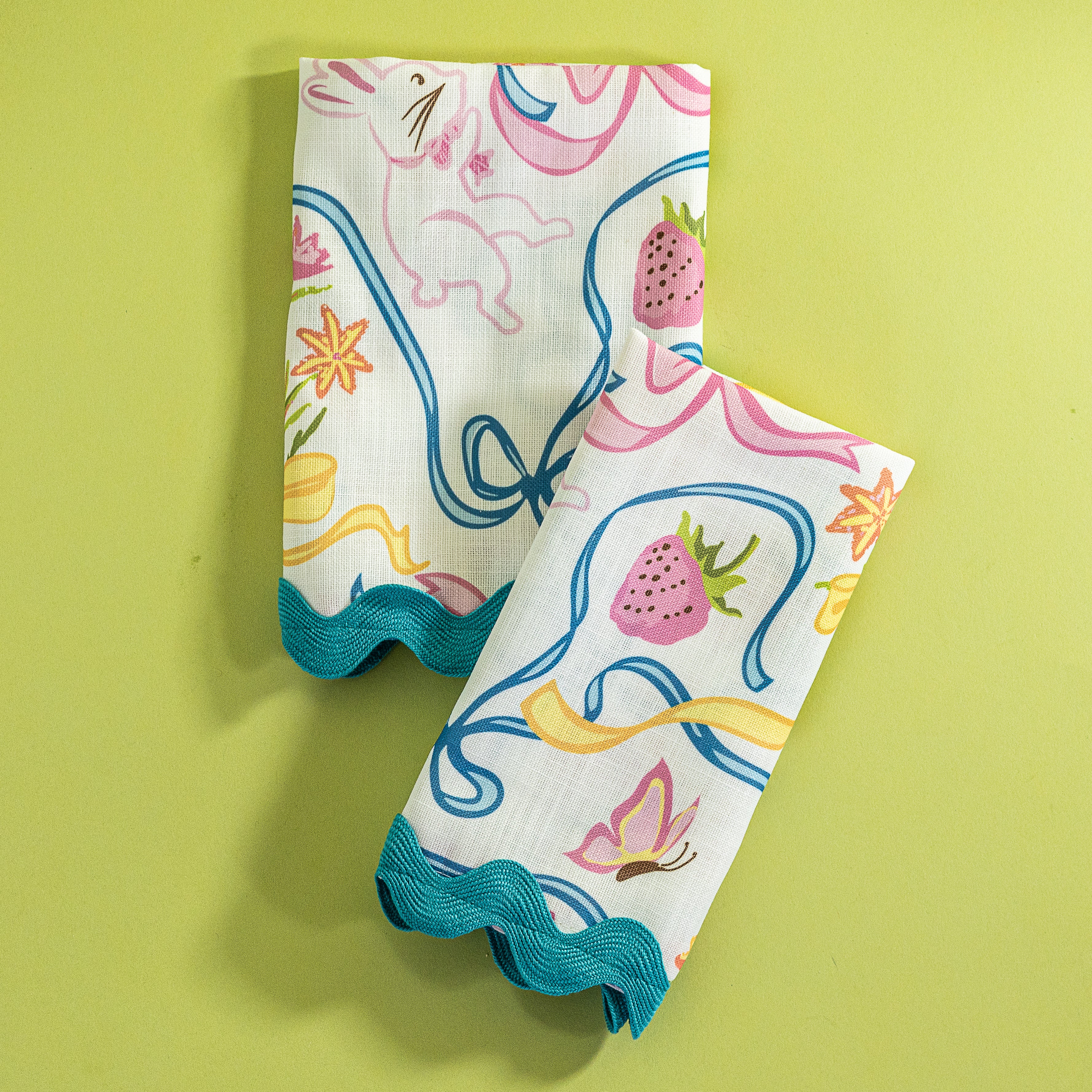 A pair of folded Bunnies and Bows print cloth dinner napkins in multicolor against a light green background.