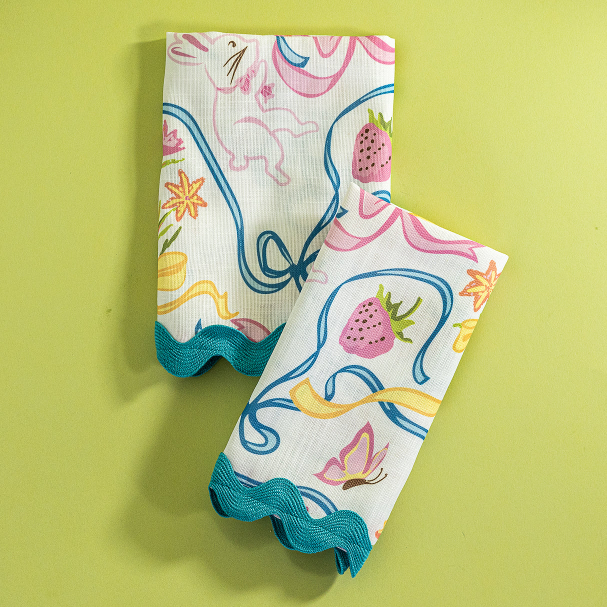 A pair of folded Bunnies and Bows print cloth dinner napkins in multicolor against a light green background.