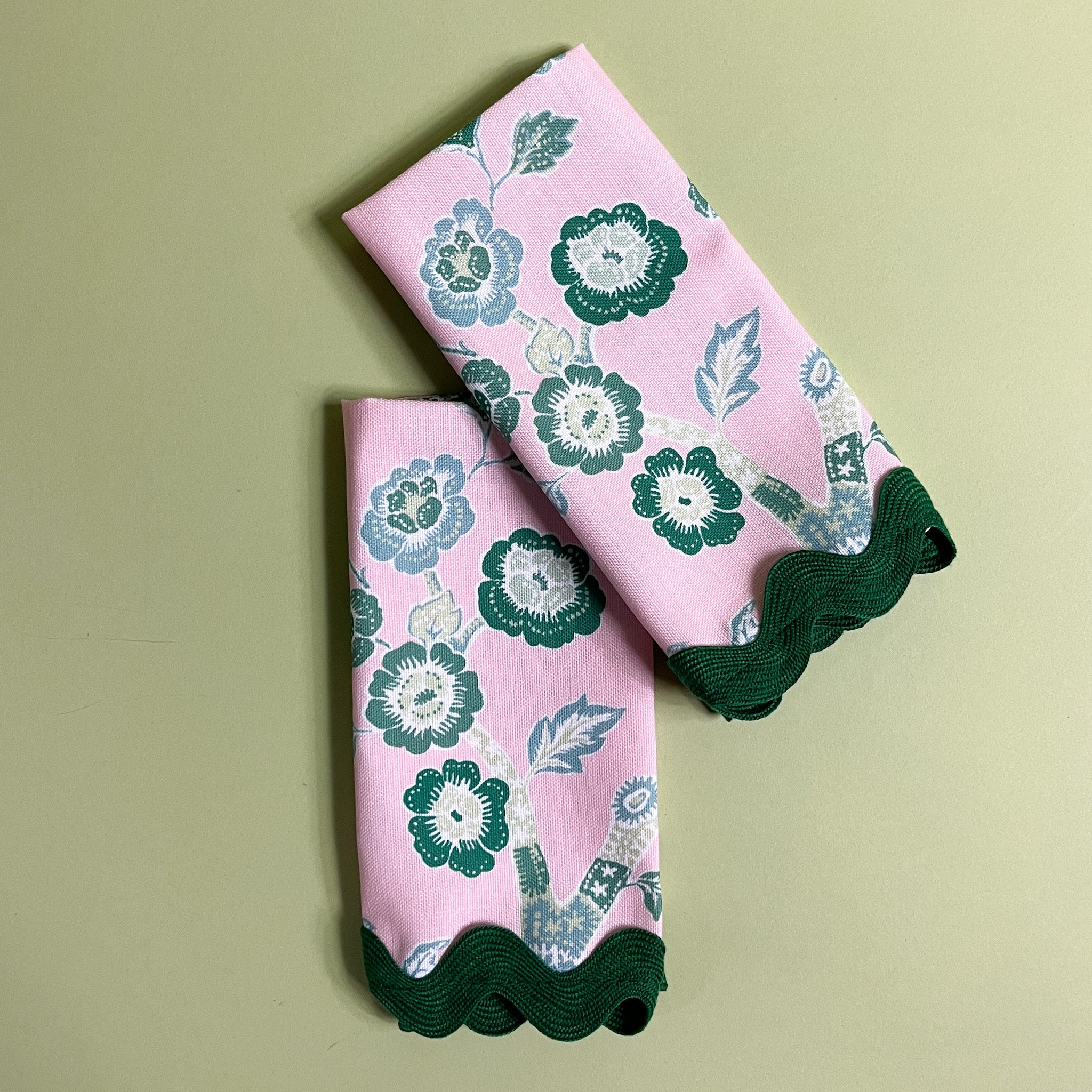 Pair of pink and green chinoiserie cloth dinner napkins in temple garden print madcap cottage fabric with ric rac trim against a light green background